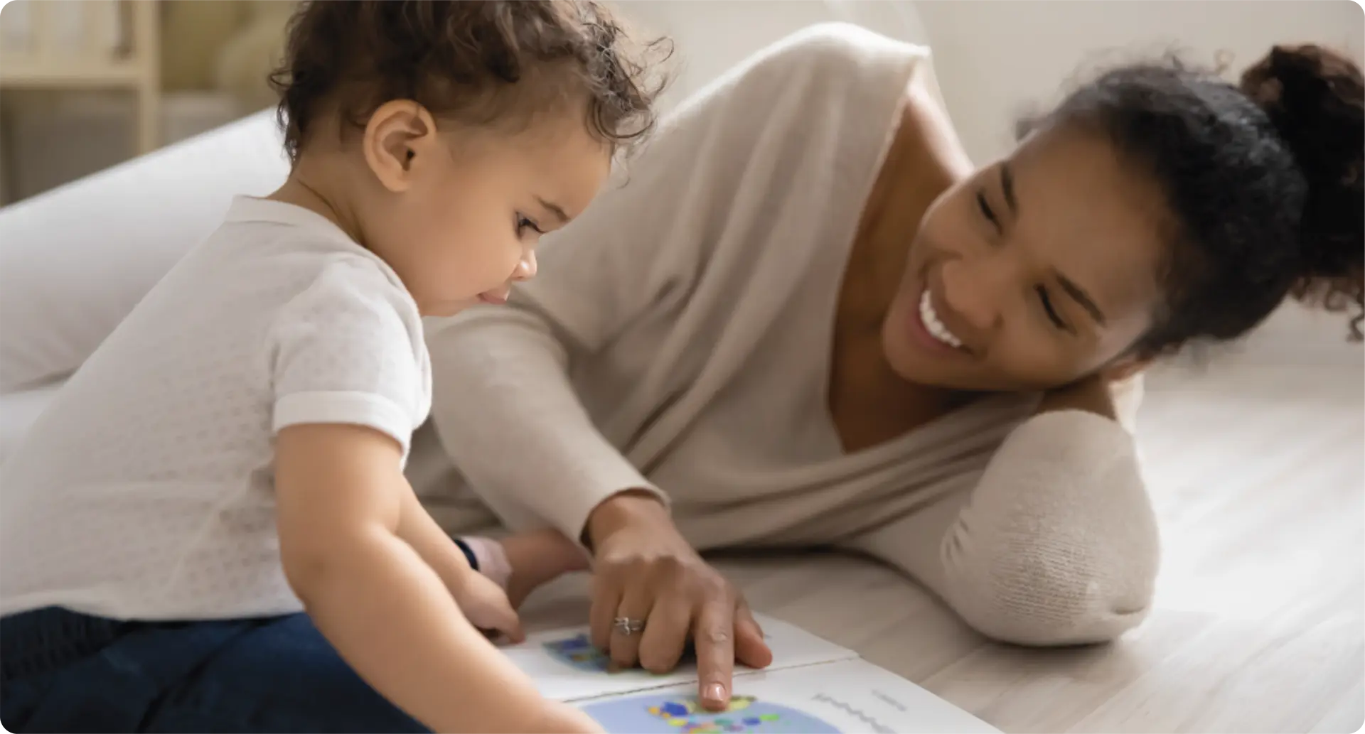 A mother smiling and reading a book with a baby